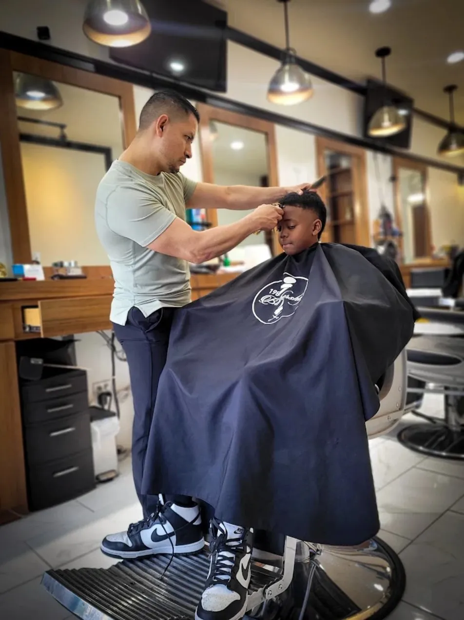 Manny cutting a young client's hair inside 1984 Barbershop